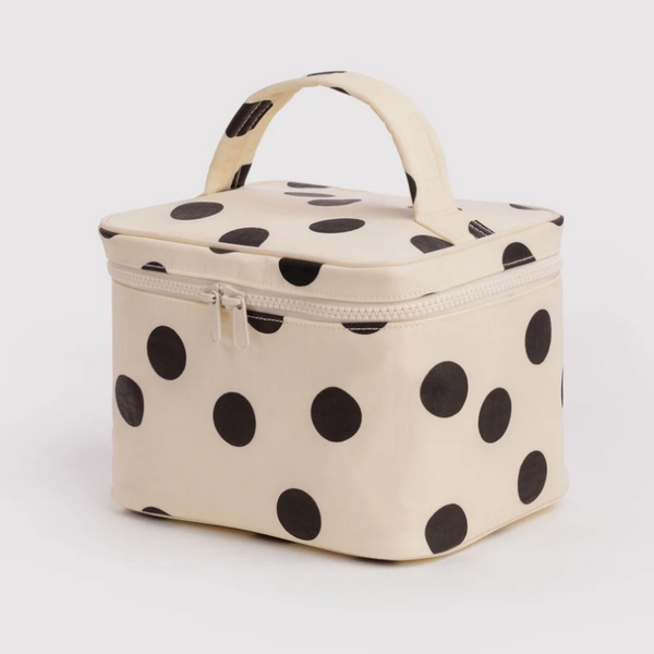 A cream-colored zippered cosmetic bag with black polka dots and a top handle, photographed on a light gray background.